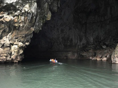 Small boat with people entering the massive Tham Kong Lo cave on calm, dark cave waters
