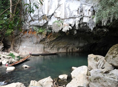 Wooden canoes docked at the entrance of Tham Kong Lo cave surrounded by large rocks